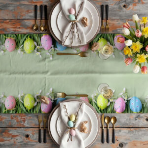 Aranżacja stołu z zastawą i bieżnikiem, pisanki w trawie wzdłuż krawędzi tworzą wielkanocną dekorację