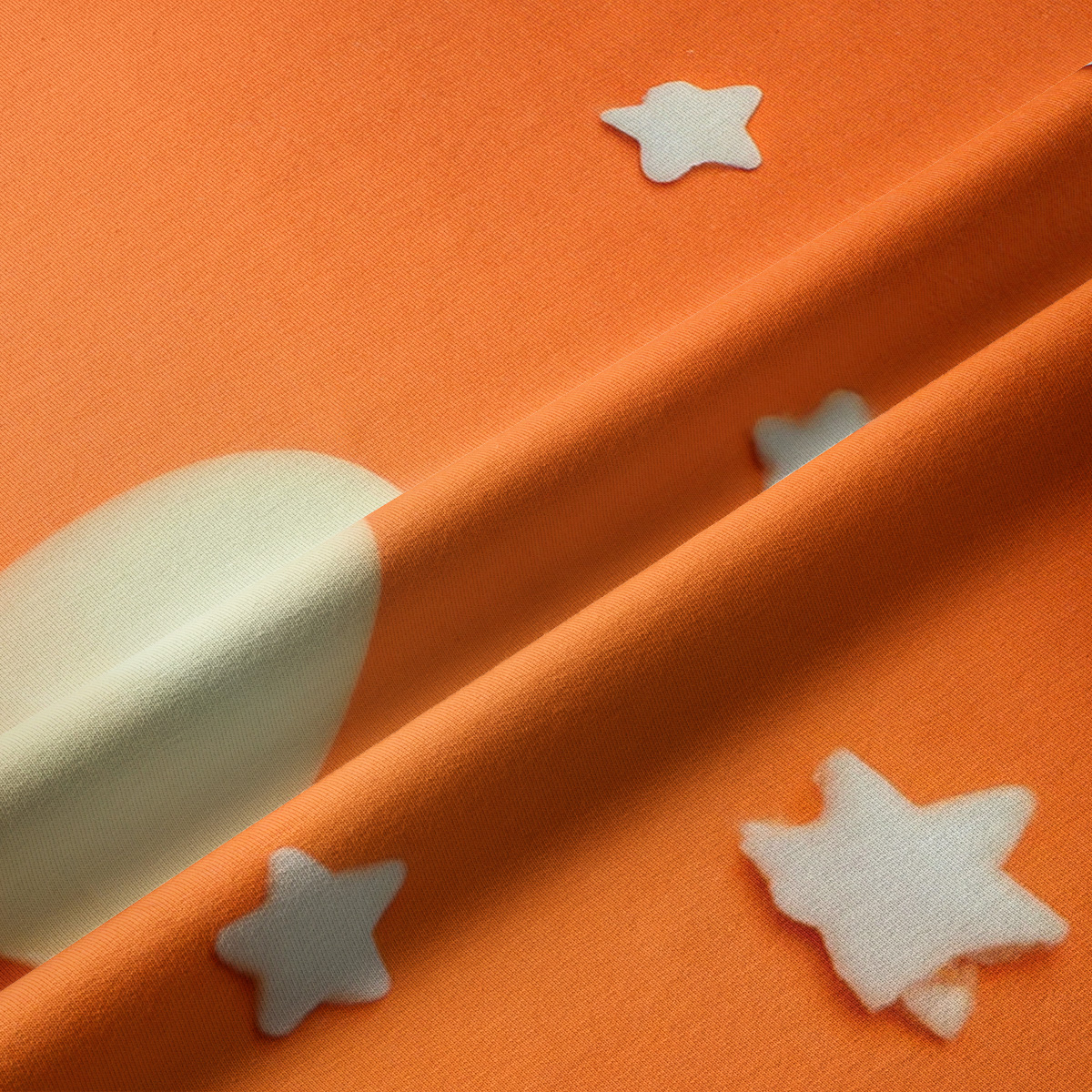 Zbliżenie na tkaninę z kremową pisanką i gwiazdką na pomarańczowym tle