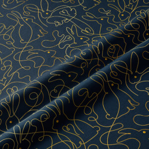 Zbliżenie na złotą kreskę tworzącą kontury zajączków na granatowej tkaninie