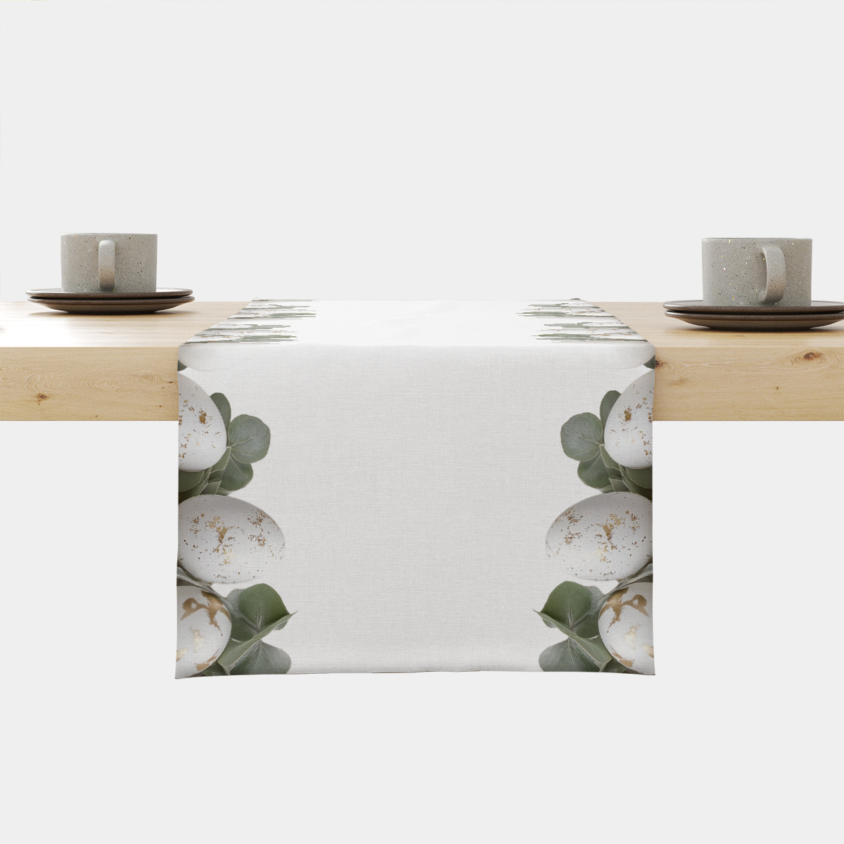 biały bieżnik z motywem białych pisanek ze złotymi plamkami i gałązkami eukaliptusa na stole