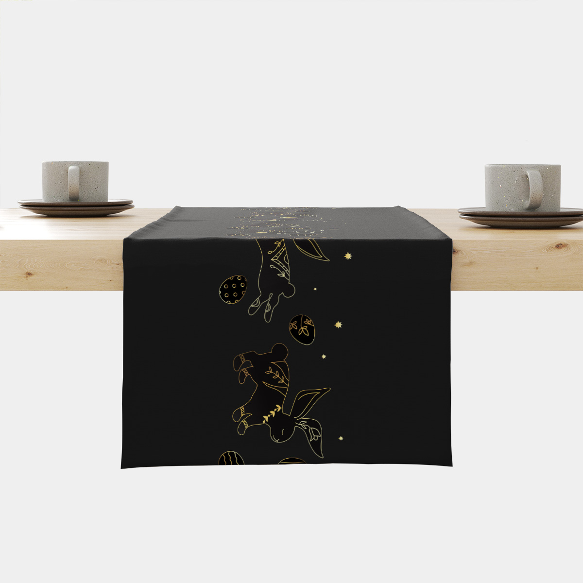 Czarny bieżnik z wzorem złotych zajączków i pisanek ułożony na drewnianym stole z zastawą