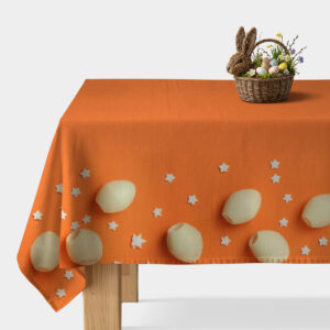 Pomarańczowy obrus z kremowymi pisankami i drobnymi białymi gwiazdkami na stole z koszykiem wielkanocnym