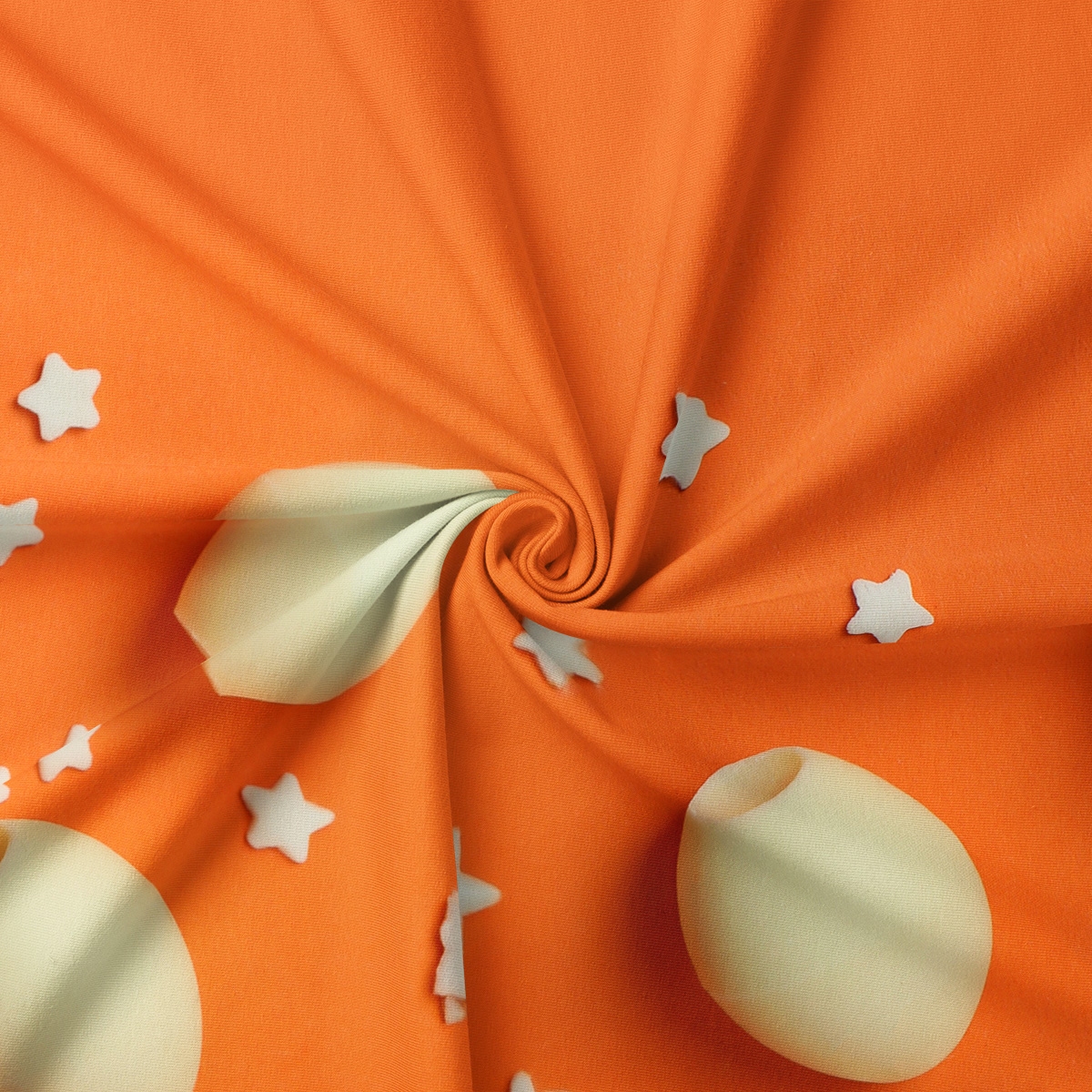 Zbliżenie na tkaninę pokazujące kremowy motyw pisanki i małe gwiazdki na pomarańczowym tle