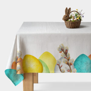 Biały obrus z kolorowymi pisankami i delikatnymi gałązkami bazi na brzegu stołu, aranżacja z koszykiem z jajkami