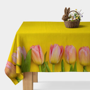 Obrus z różowymi tulipanami na żółtym tle rozłożony na stole z koszykiem wielkanocnym