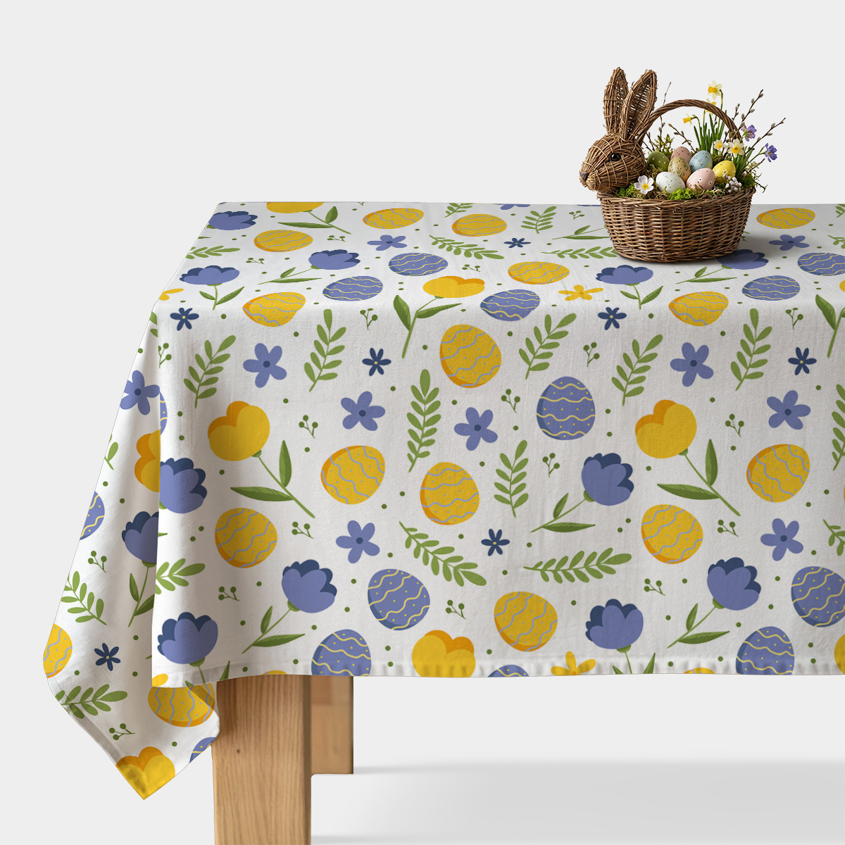 Obrus na stole z żółtymi i niebieskimi pisankami oraz wiosennymi kwiatami na białym tle