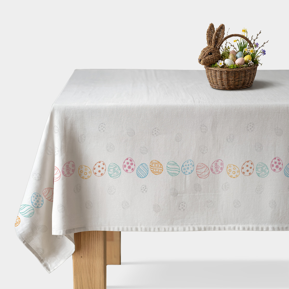 biały obrus z pasem kolorowych pisanek na stole i koszykiem z dekoracjami