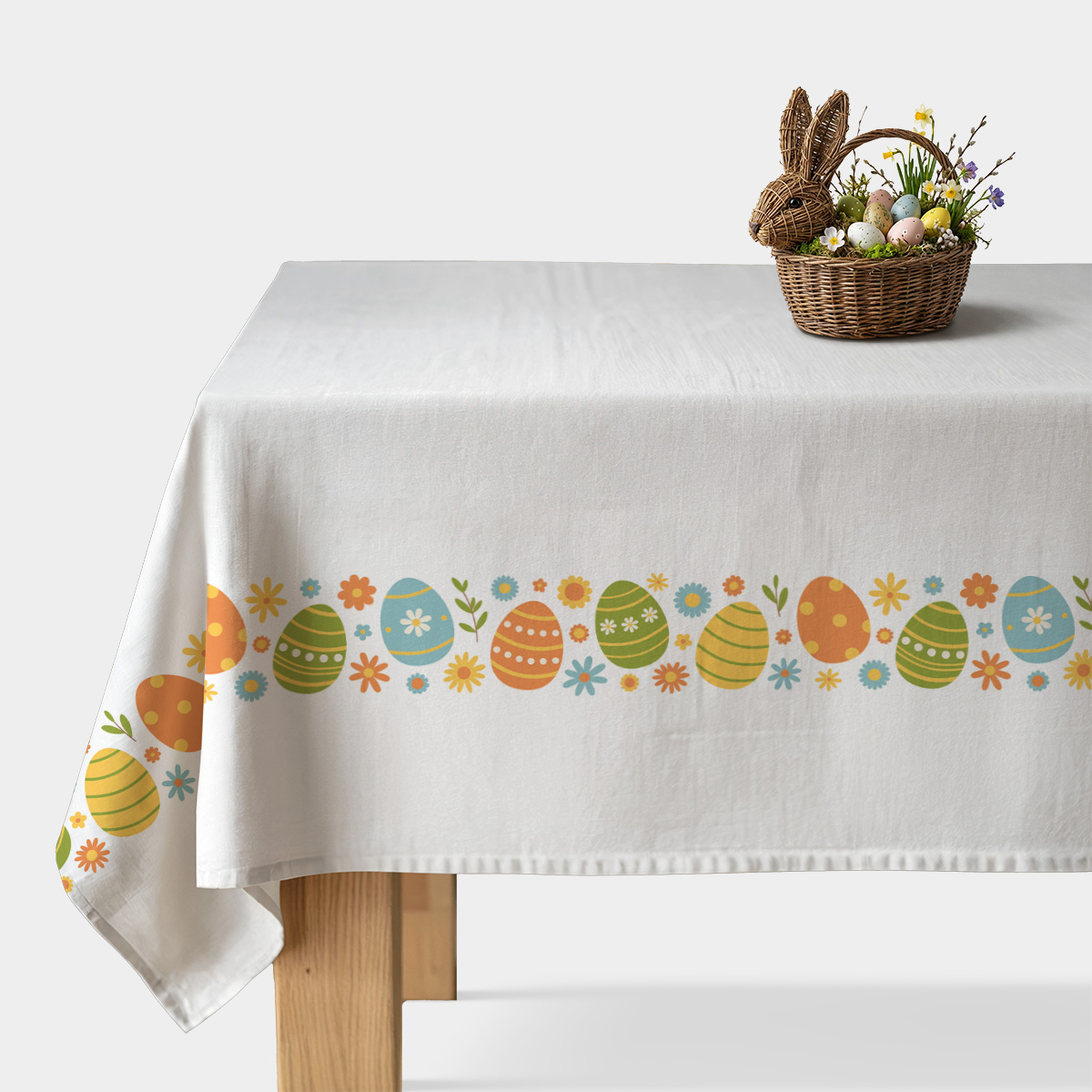 biały obrus z poziomym pasem kolorowych pisanek i kwiatków na stole z koszykiem ozdobnych jajek