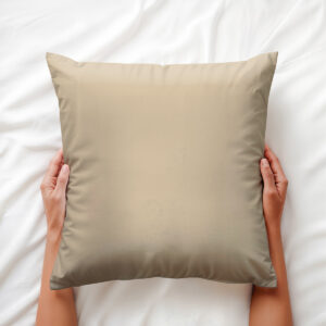 Widok z góry na poduszkę trzymaną dłońmi na białej pościeli