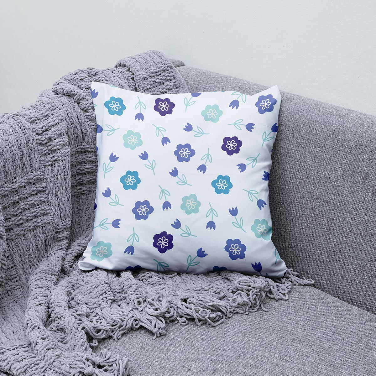 Poduszka ułożona na szarej sofie obok pledu jako stylowa aranżacja wnętrza