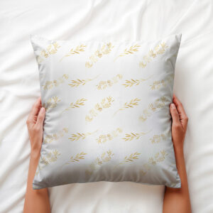 widok poduszki trzymanej w dłoniach na pościeli, złote gałązki na jasnym tle
