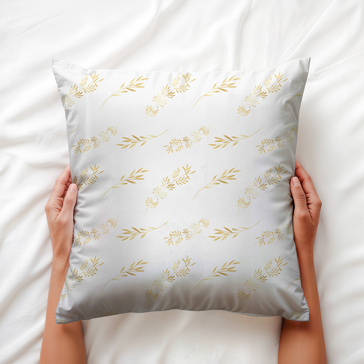 widok poduszki trzymanej w dłoniach na pościeli, złote gałązki na jasnym tle