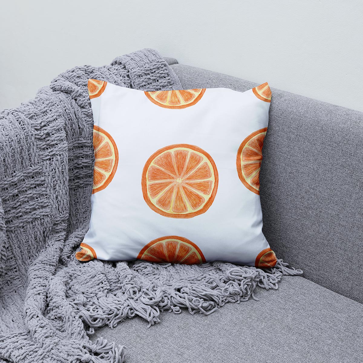 poduszka z powtarzającym się wzorem pomarańczy ułożona na sofie obok miękkiego koca