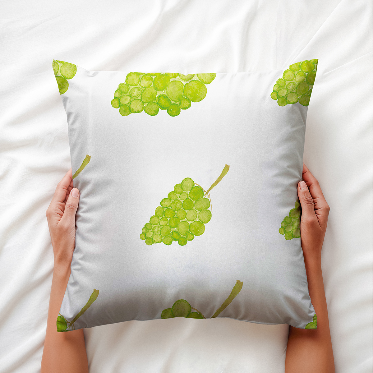 Ręce trzymające poduszkę z wzorem akwarelowych winogron, widoczny detal nadruku i faktura materiału