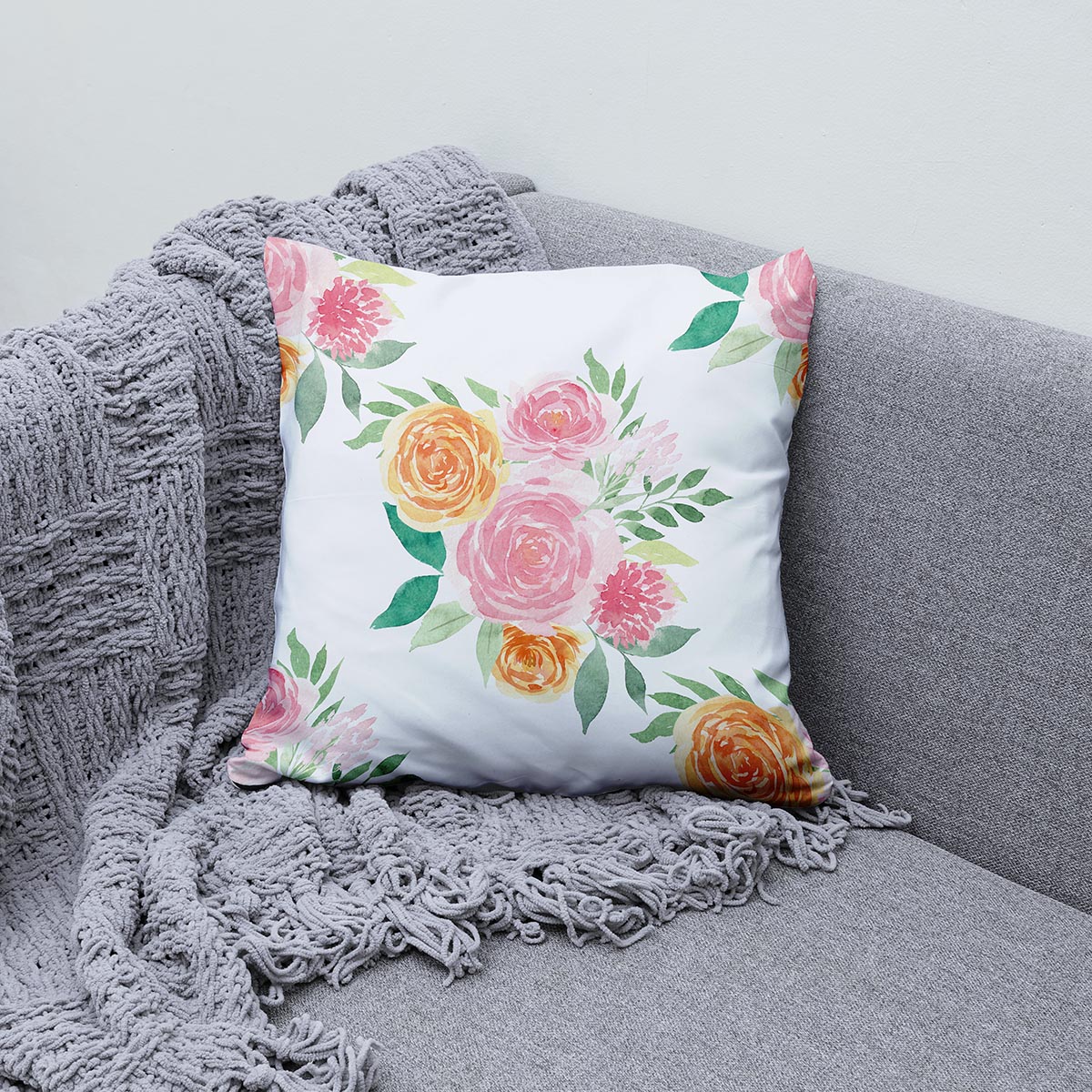 aranżacja poduszki na szarej kanapie z pledem, widoczny wzór akwarelowych kwiatów