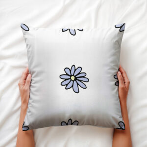Poduszka trzymana w dłoniach na pościeli, widoczny centralny motyw stokrotki