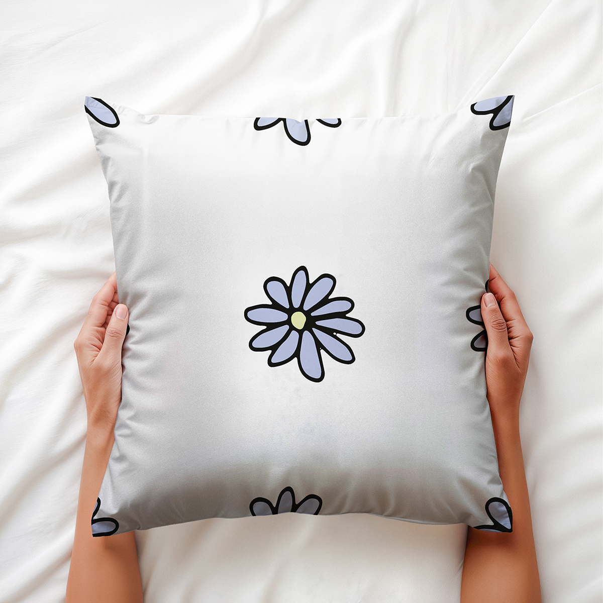 Poduszka trzymana w dłoniach na pościeli, widoczny centralny motyw stokrotki