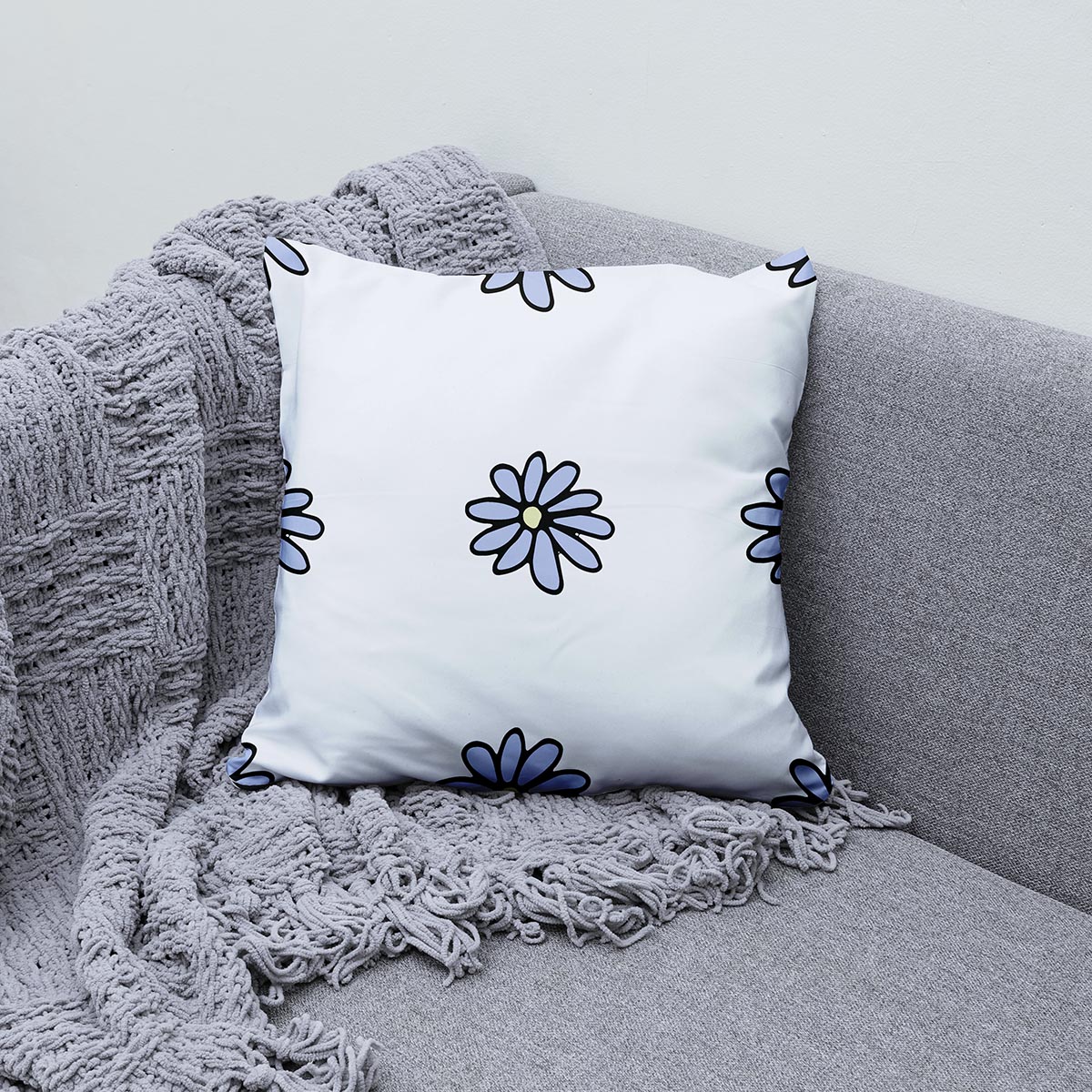 Poduszka ozdobna z motywem stokrotek ułożona na kanapie obok pledu