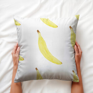 Dłoń trzyma poduszkę z motywem bananów, widoczna faktura tkaniny i nasycenie koloru
