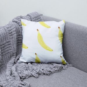 Poduszka z bananowym wzorem ułożona na szarej sofie i pledzie jako przytulna aranżacja