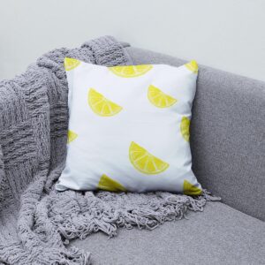 Poduszka z motywem cytryny ułożona na szarej sofie obok pledu
