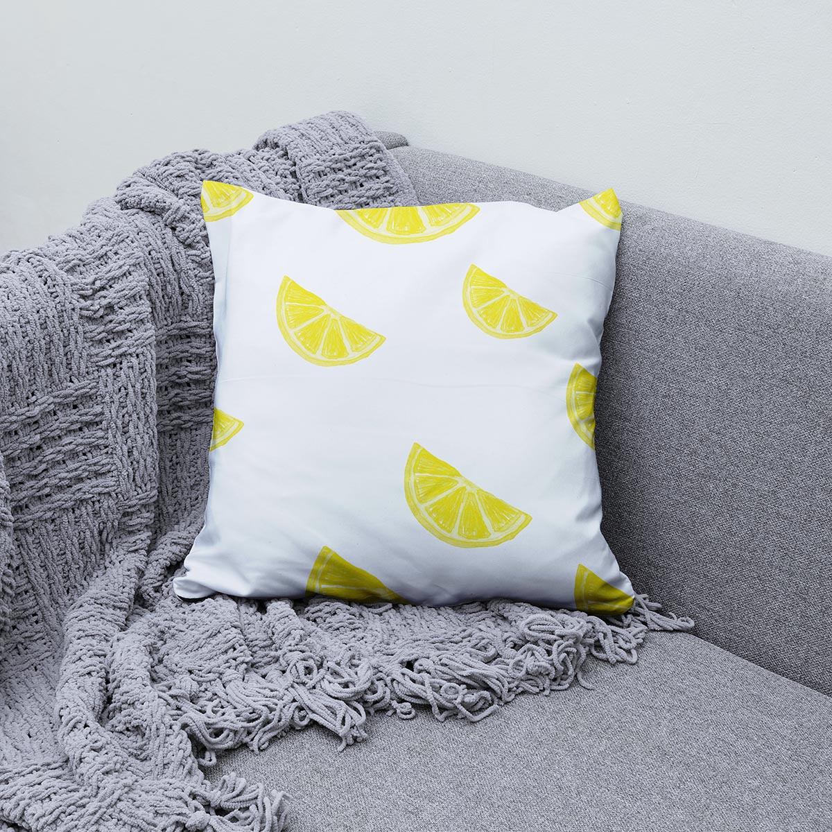 Poduszka z motywem cytryny ułożona na szarej sofie obok pledu