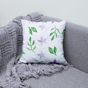 Poduszka ozdobna z delikatnym akwarelowym wzorem ułożona na szarej sofie obok pleda