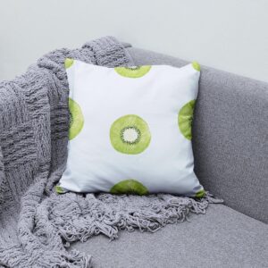 Poduszka z plasterkiem kiwi ułożona na szarej sofie obok plecionego koca jako aranżacja wnętrza