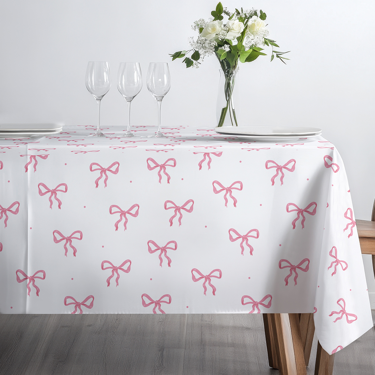 Widok z boku na stół udekorowany kieliszkami i bukietem na obrusie z motywem kokard