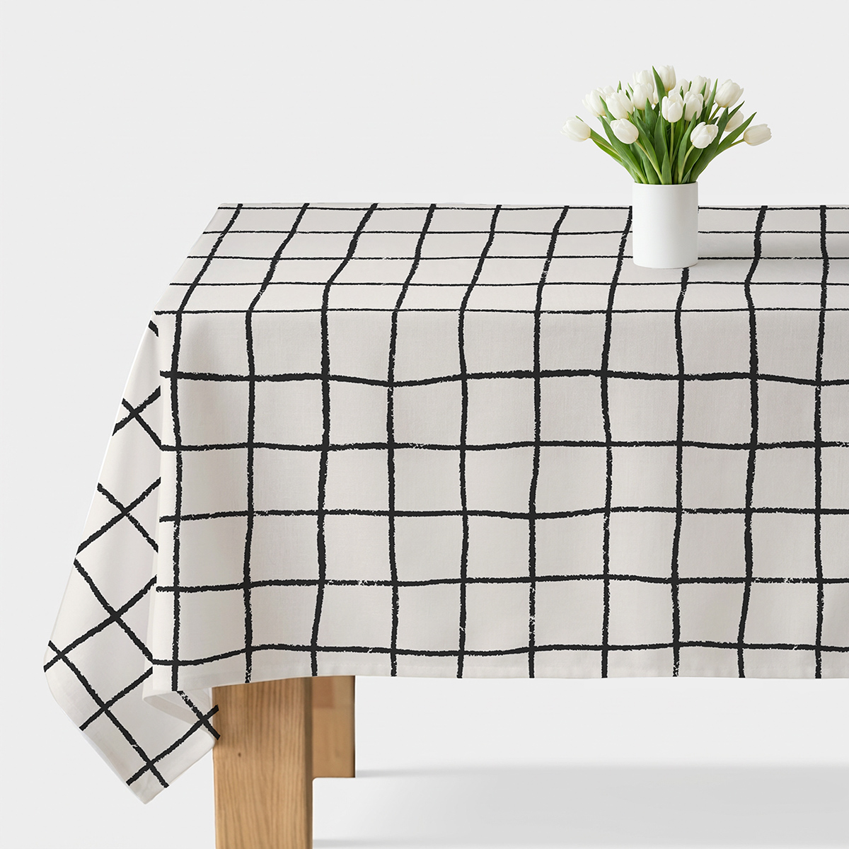 stół z obrusem w ręcznie malowaną czarną kratę i biały wazon z tulipanami