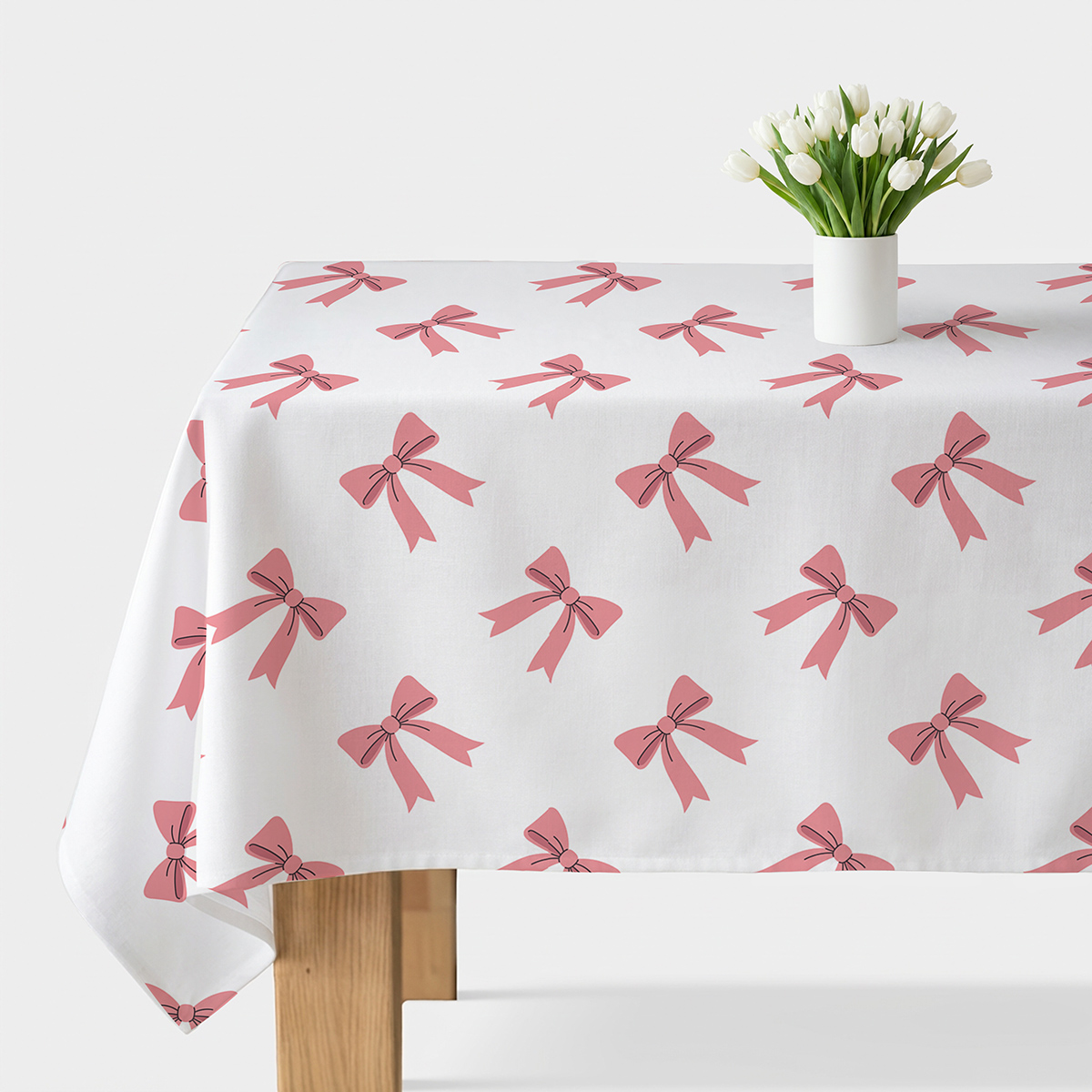 obrus z różowymi kokardkami rozłożony na stole z białym wazonem i tulipanami