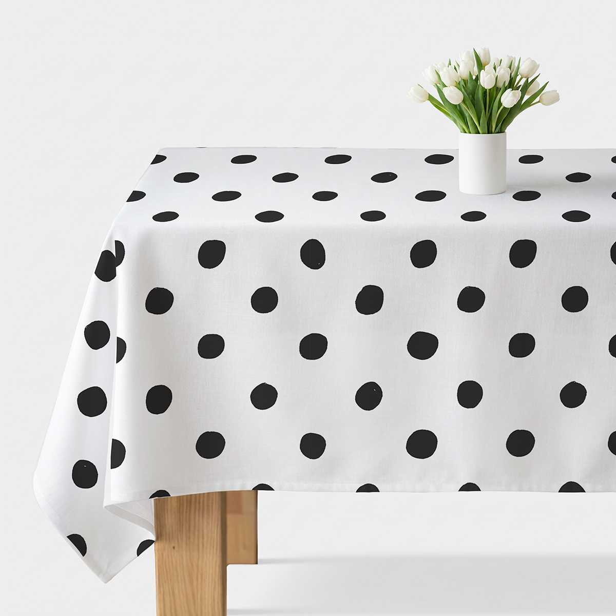 biały obrus w czarne malowane kropki rozłożony na drewnianym stole z wazonem białych tulipanów