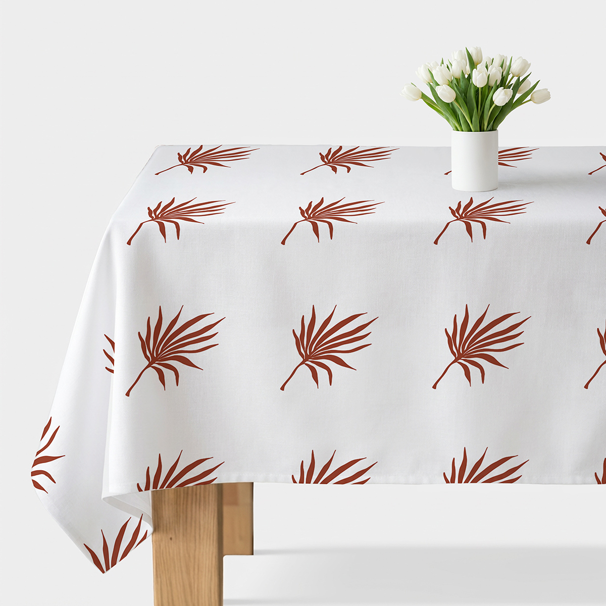 obrus na stole z białym tłem i powtarzalnym wzorem palmowych liści w kolorze ceglastym, widok frontalny