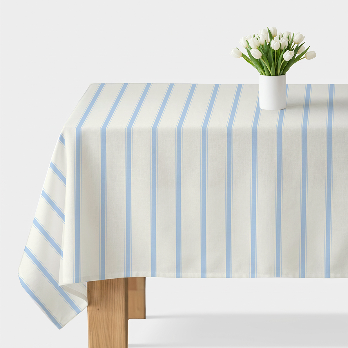 Obrus kremowy z pionowymi błękitnymi pasami na stole z wazonem białych tulipanów