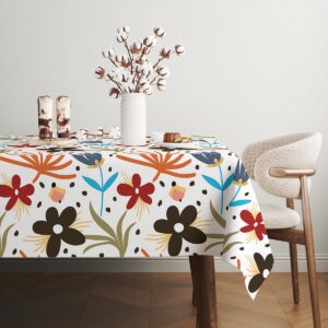 stół udekorowany obrusem w kwiatowy wzór z ceramicznym wazonem i talerzami na jasnym tle