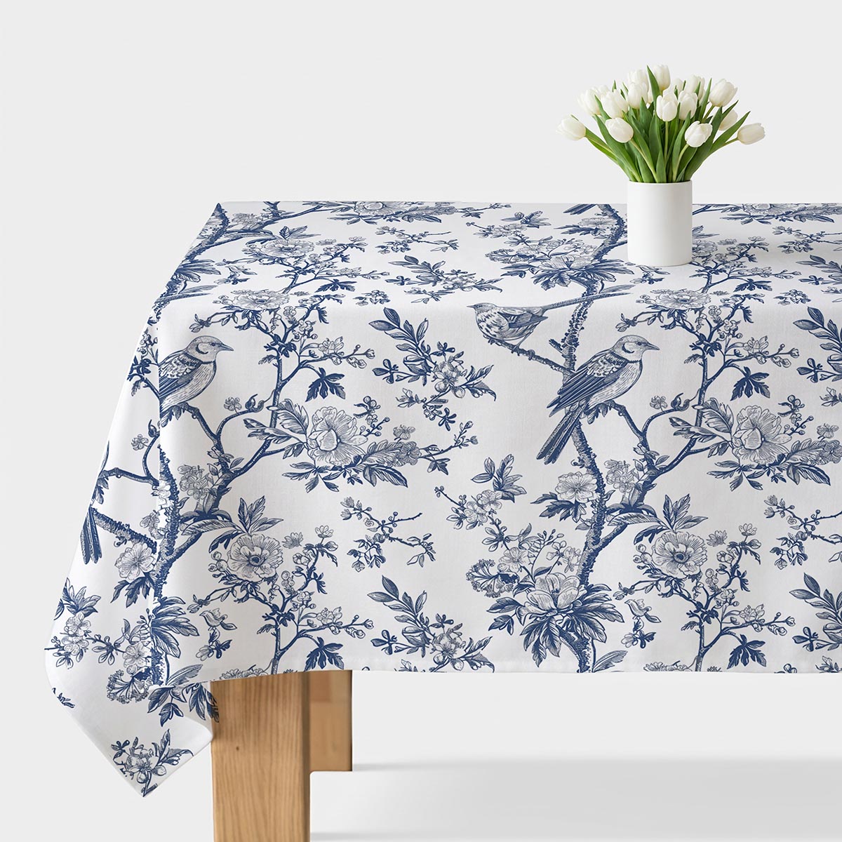 biało-niebieski obrus z ptakami i gałązkami na stole z wazonem tulipanów