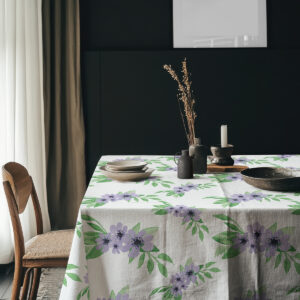 Aranżacja stołu z obrusem w fioletowe kwiaty na tle ciemnej ściany i ceramicznymi naczyniami