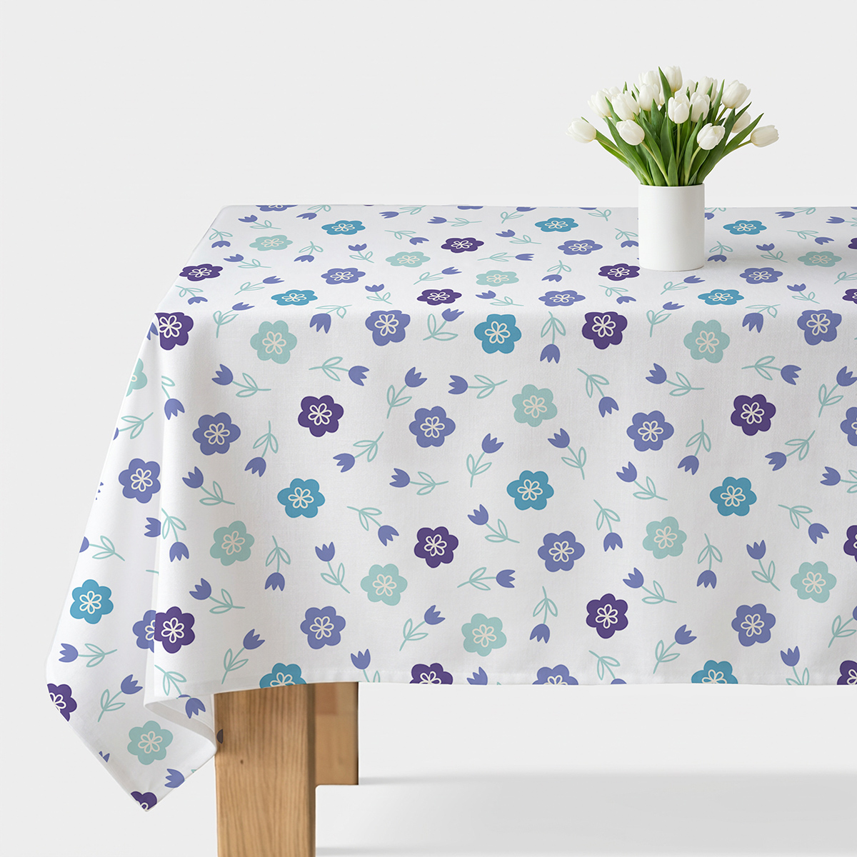 Obrus na stole z jasnym tłem i drobnym wzorem turkusowo-fioletowych kwiatków z wazonem białych tulipanów