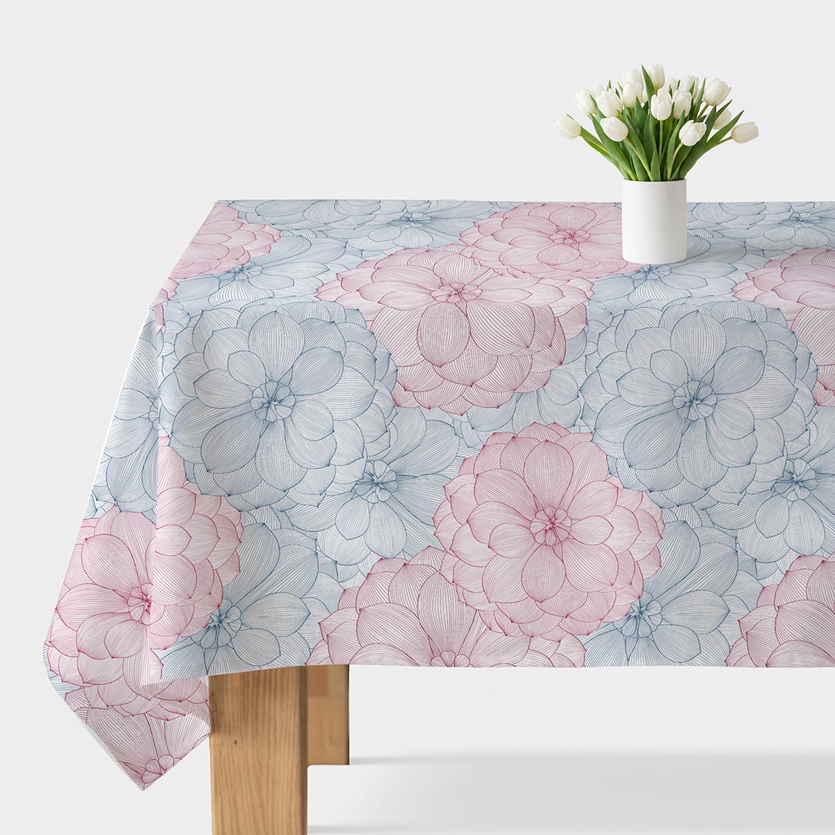 Obrus z dużymi szkicowymi kwiatami w pastelowych odcieniach różu i błękitu rozłożony na stole z wazonem tulipanów