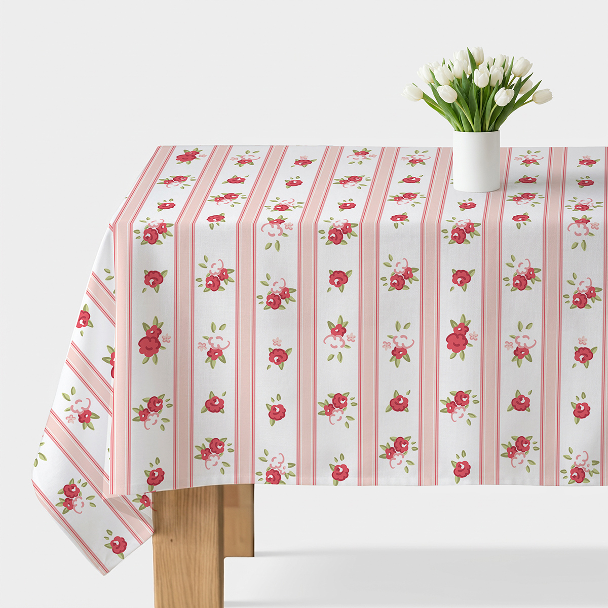 Stół przykryty obrusem z pionowymi różowymi pasami i drobnymi czerwonymi różyczkami