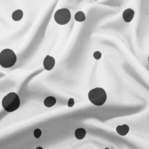 Zbliżenie tkaniny pokazujące nieregularne czarne kropki i delikatną fakturę materiału
