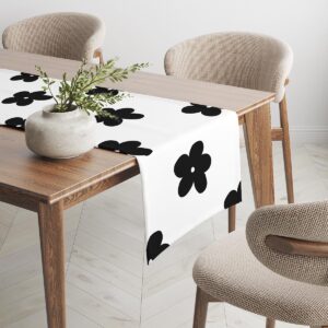 bieżnik rozłożony na drewnianym stole z dekoracyjną donicą i krzesłami w tle