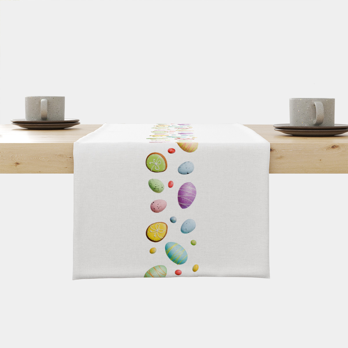 Bieżnik z pionowym pasem pastelowych pisanek i ciasteczek rozłożony na jasnym stole, widok frontalny