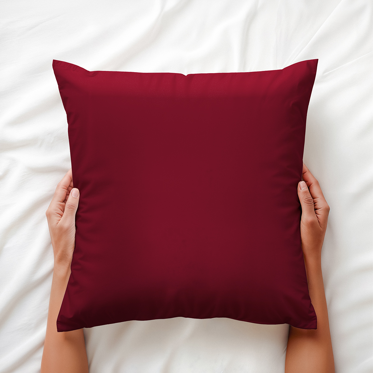 Ręce trzymające bordową poduszkę na białej pościeli, ujęcie z góry