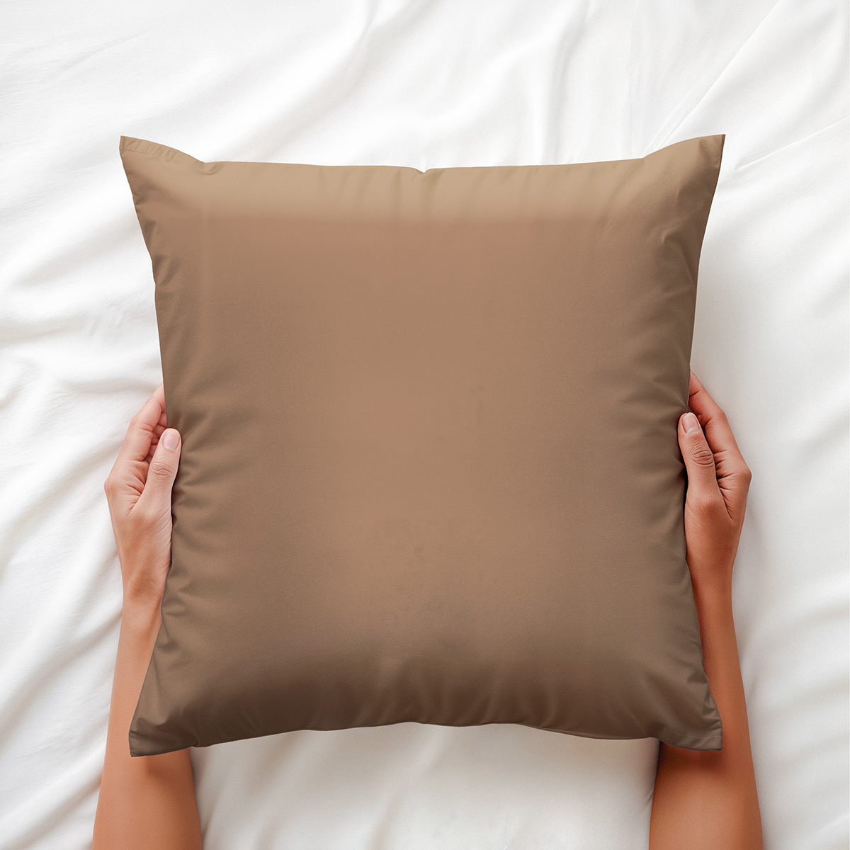 karmelowa poduszka dekoracyjna trzymana dłońmi na pościeli ujęcie z góry