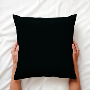 czarna poduszka ozdobna trzymana dłońmi na jasnej pościeli, ujęcie z góry