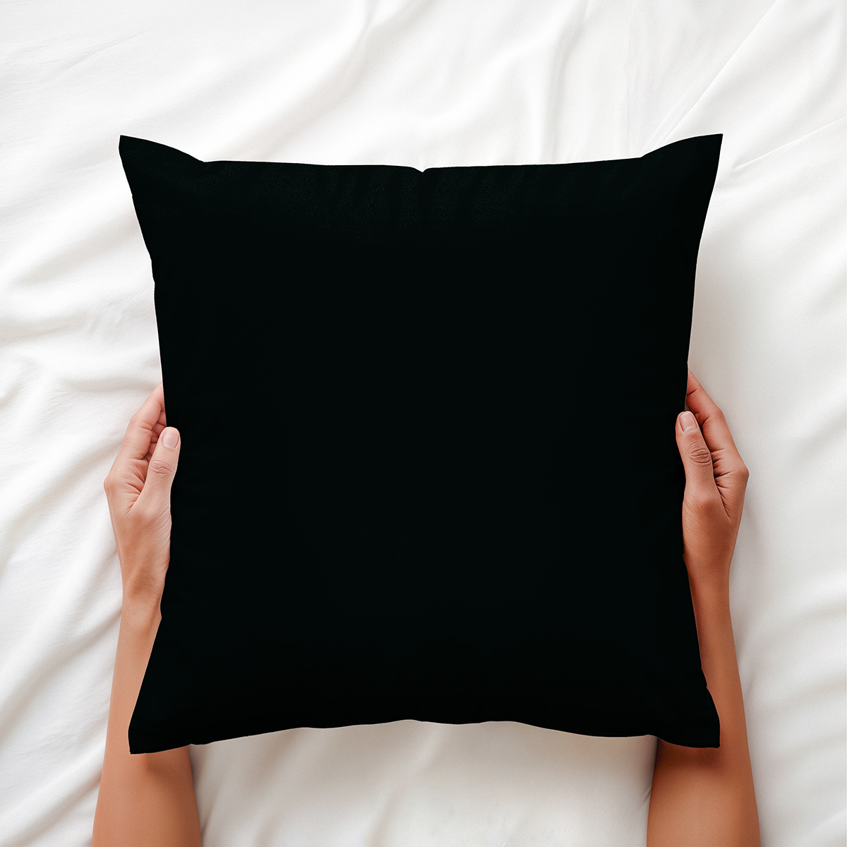 czarna poduszka ozdobna trzymana dłońmi na jasnej pościeli, ujęcie z góry