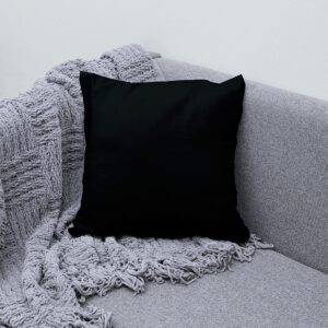 czarna poduszka na kanapie obok plecionego szarego koca, aranżacyjne ujęcie