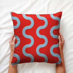 ręce trzymające poduszkę z błękitnymi falami na czerwonym tle, ujęcie aranżacyjne