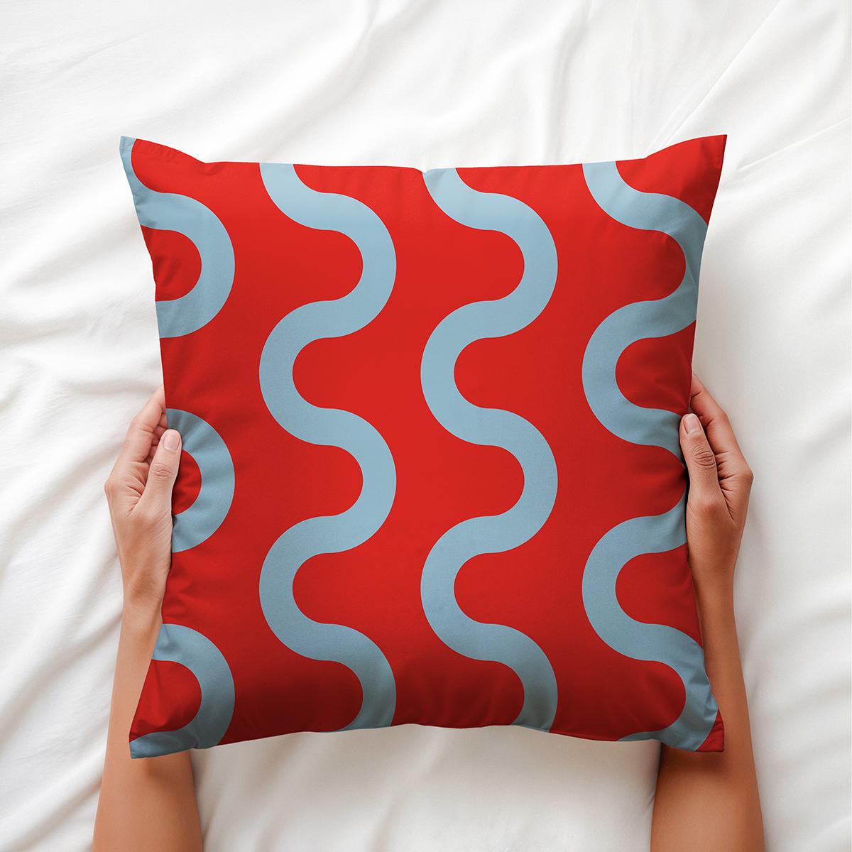 ręce trzymające poduszkę z błękitnymi falami na czerwonym tle, ujęcie aranżacyjne